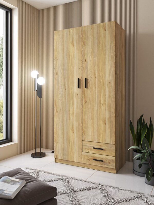 Armario de 2 puertas y 2 cajones modelo Aura en color beig con tiradores negros, instalado en un dormitorio luminoso.