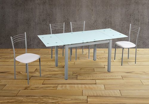Conjunto de mesa 70 de cristal templado con patas metálicas y 4 sillas 20 tapizadas en polipiel blanca, ubicado en una cocina moderna y luminosa.