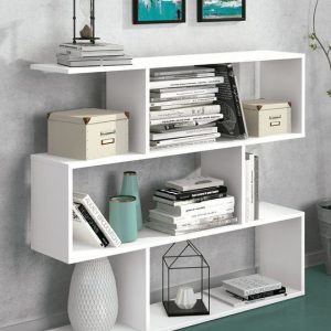 Estantería Aura Asimétrica Baja en color blanco con libros y objetos decorativos en un salón moderno.