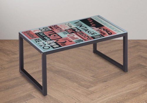 Mesa de centro para salón fija modelo Danubio, rectangular con tapa de cristal y collage gráfico, frente a un sofá en un salón moderno.
