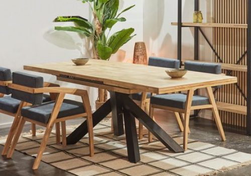 Mesa de comedor extensible de madera maciza para 8 a 10 personas, con patas de forja, desplegada en un comedor familiar, rodeada de invitados disfrutando de una cena animada.