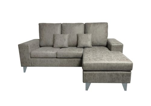 El sofá chaise longue reversible Duque en color cemento, mostrado en un salón luminoso con su pouf independiente.